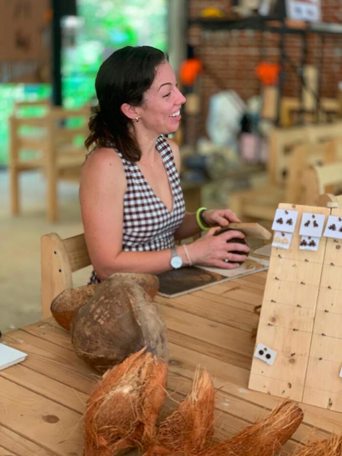 A visitor working a coconut shell beside a rack of finished earrings at the Impact Center in Sigiriya.