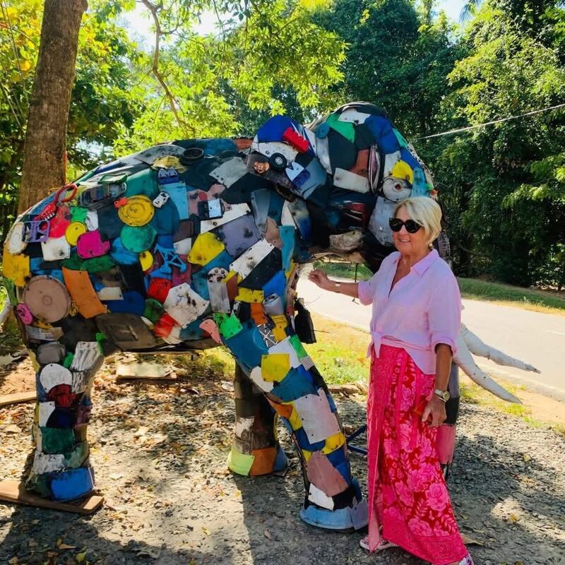 A visitor standing beside the plastic elephant in the morning sun.