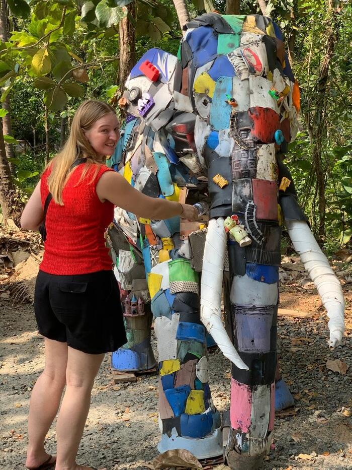 A visitor reaching out to touch the plastic elephant among the trees.