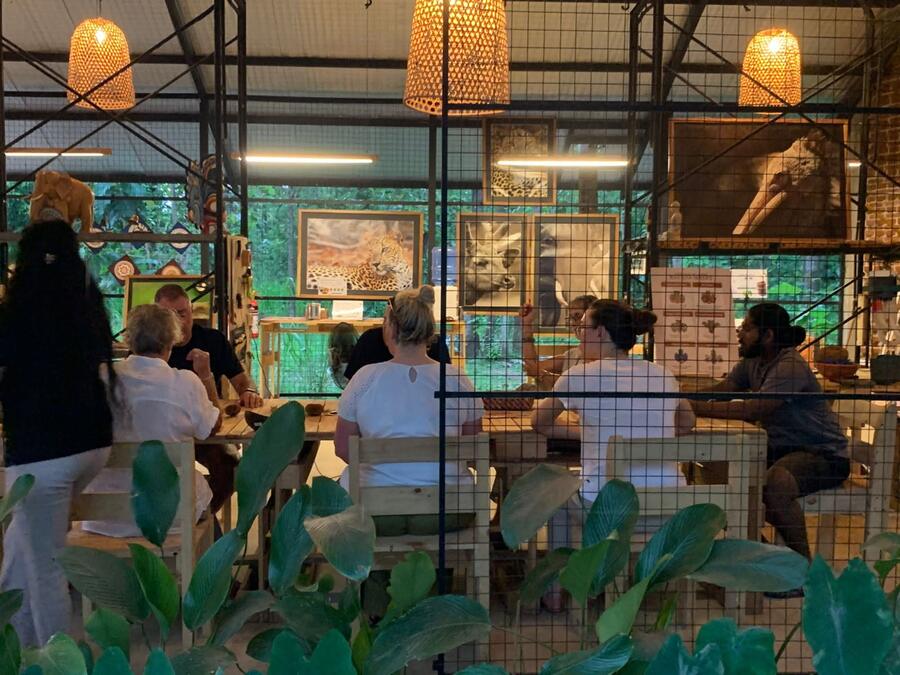 Visitors seated around the long bench in the evening, lamps lit, jungle behind.