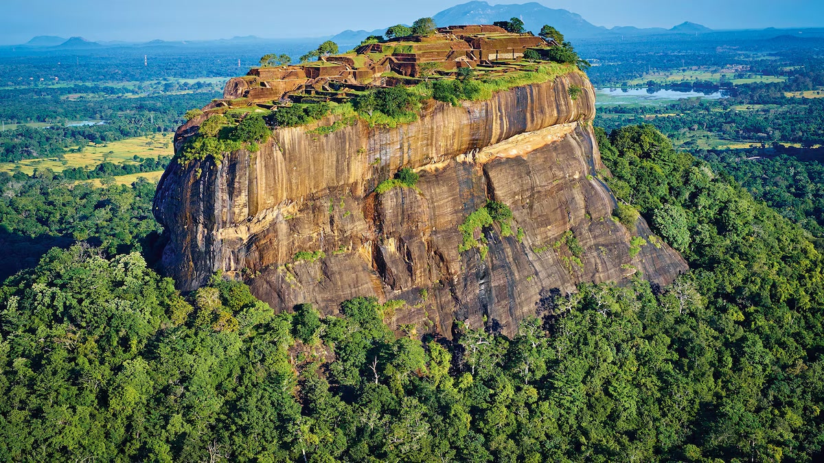 Aerial view of the sheer rock face of Sigiriya, with the summit ruins and surrounding plains visible.