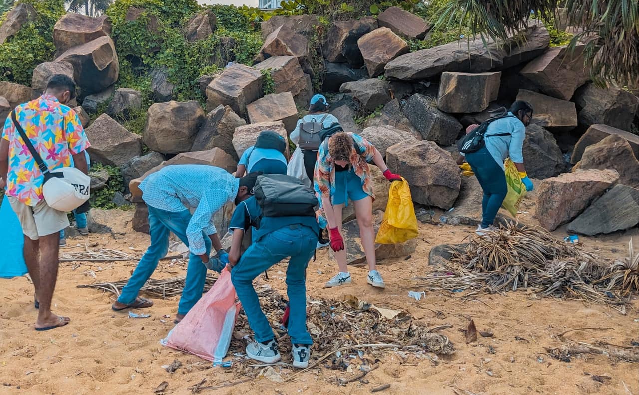 ZeroPlastic volunteers collecting plastic waste into bags among the rocks at Mount Lavinia beach, Sri Lanka.