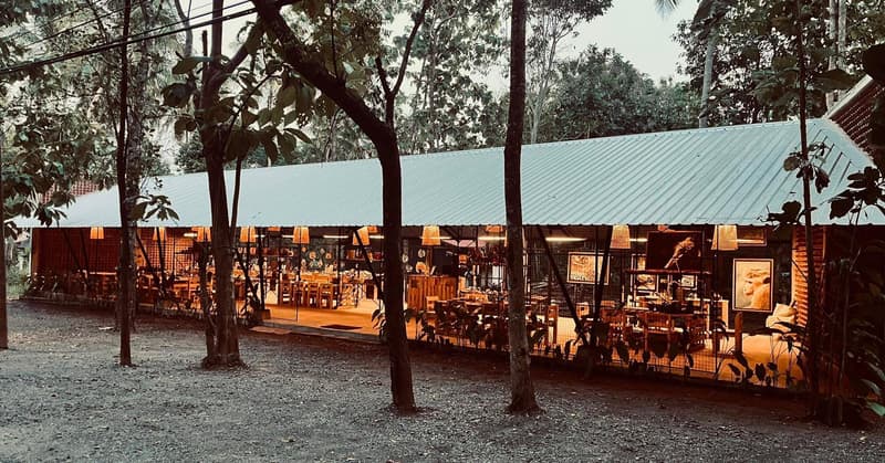 The Impact Center by ZeroPlastic in Sigiriya at dusk, an open timber pavilion lit from within and surrounded by forest.