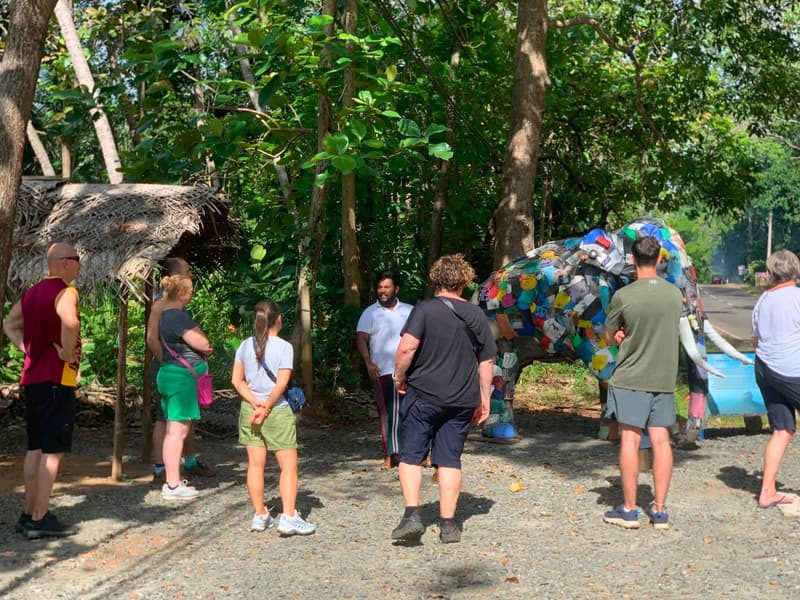 A group of visitors standing with a ZeroPlastic team member beside the salvaged-plastic elephant sculpture at the roadside in Sigiriya.