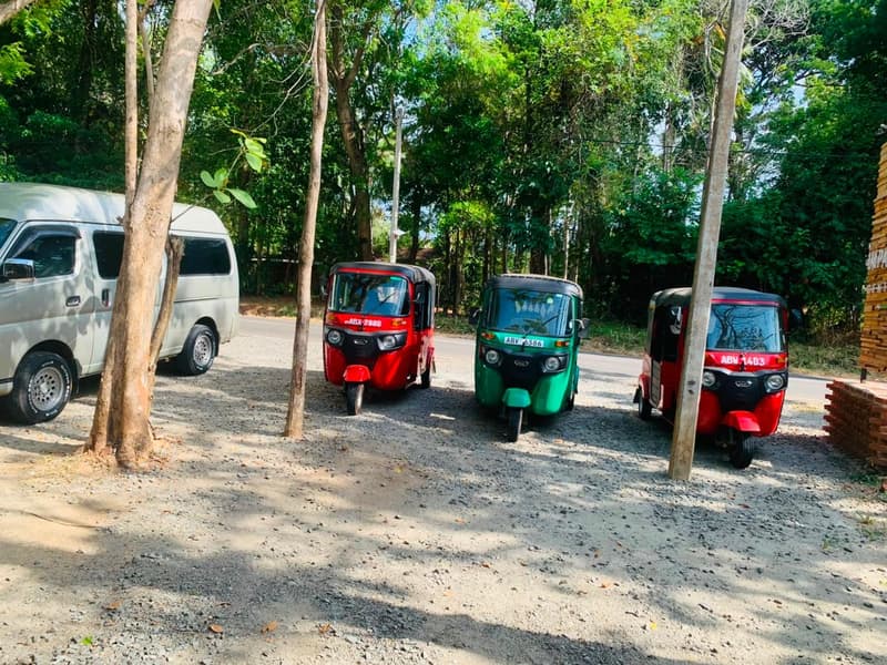 Three tuk-tuks in different colours and a van parked under trees at the ZeroPlastic Impact Center in Sigiriya.