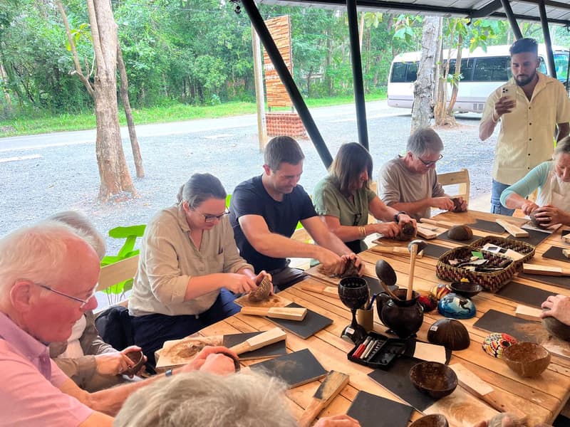 International visitors making coconut-shell craft at a workbench during an Impact Center session.
